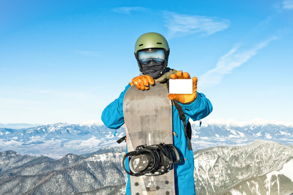 Snowboarder holding blank ski-pass with mountains on background